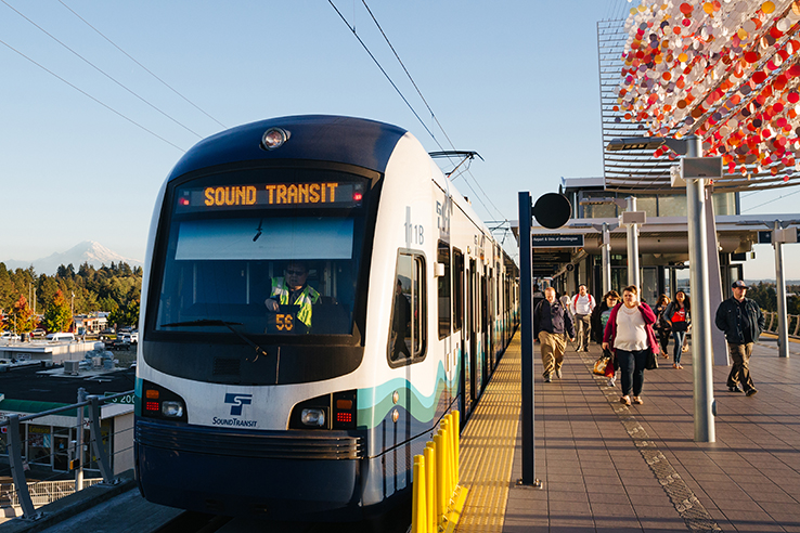 A LINK light rail train pulling into a station with passengers standing on the platform, waiting to board.