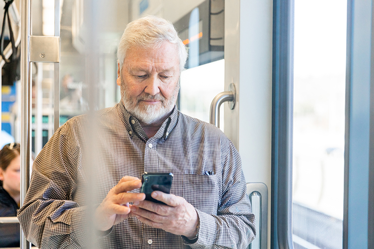 A man riding a light rail train looks down at his phone. 