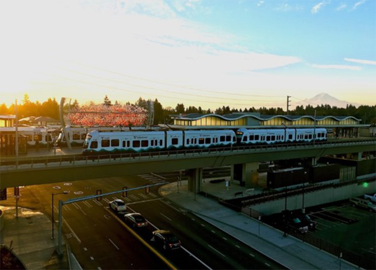 Un tren de Link light rail viaja sobre una calzada en una vía elevada, con el monte Rainier al fondo.